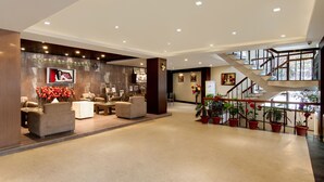 Um hall amplo com balcão de recepção, assentos confortáveis, escada e plantas em vasos.