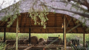 Zona de hidromasaje al aire libre de estilo rústico, con banco de madera y una estructura de techo de paja.