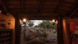Un interior de madera con un sendero de piedra que conduce a un espacio exterior con rocas y vegetación escasa.