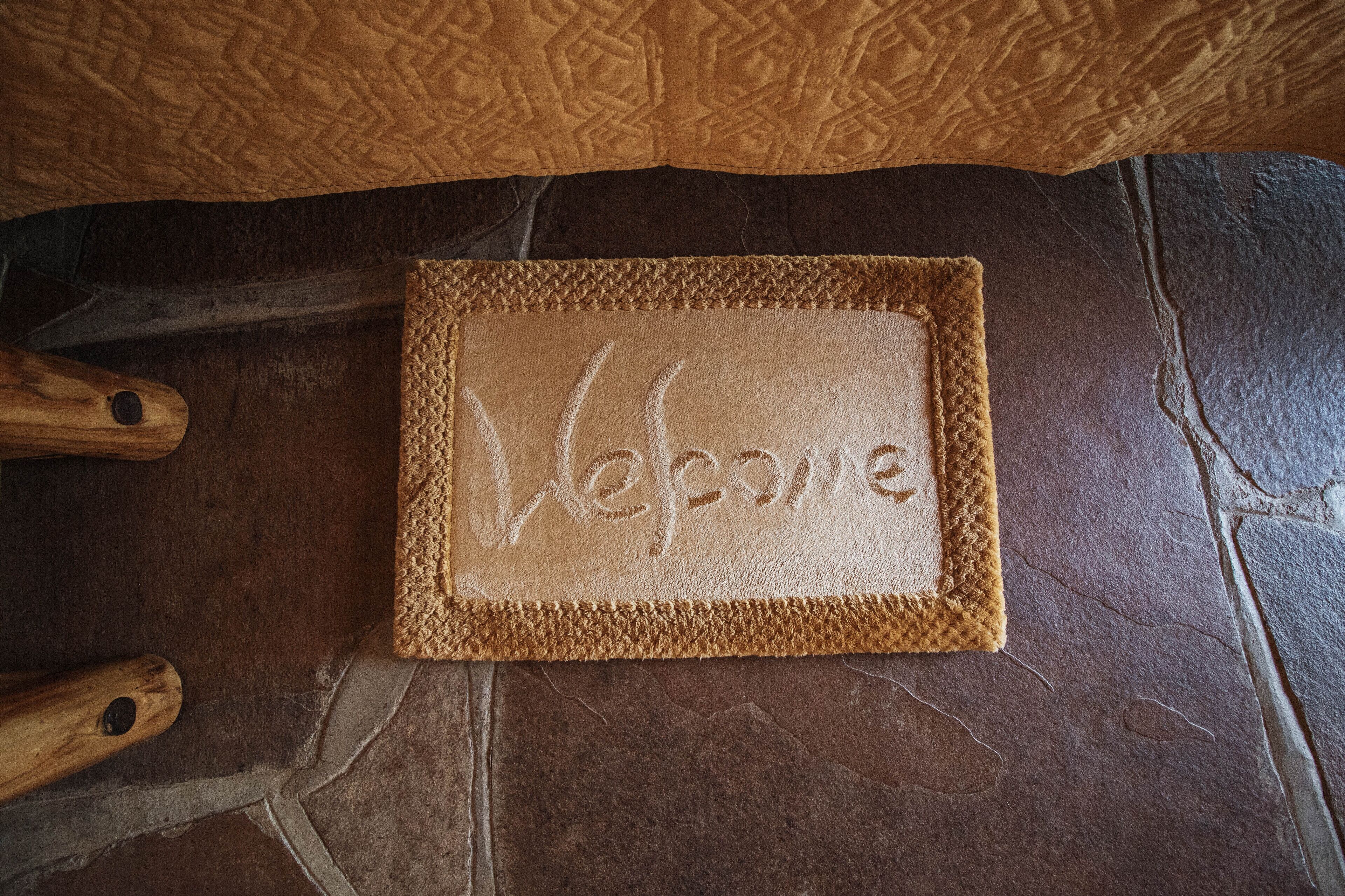Un felpudo con textura y la palabra 'Welcome' inscrita, sobre un piso de piedra.