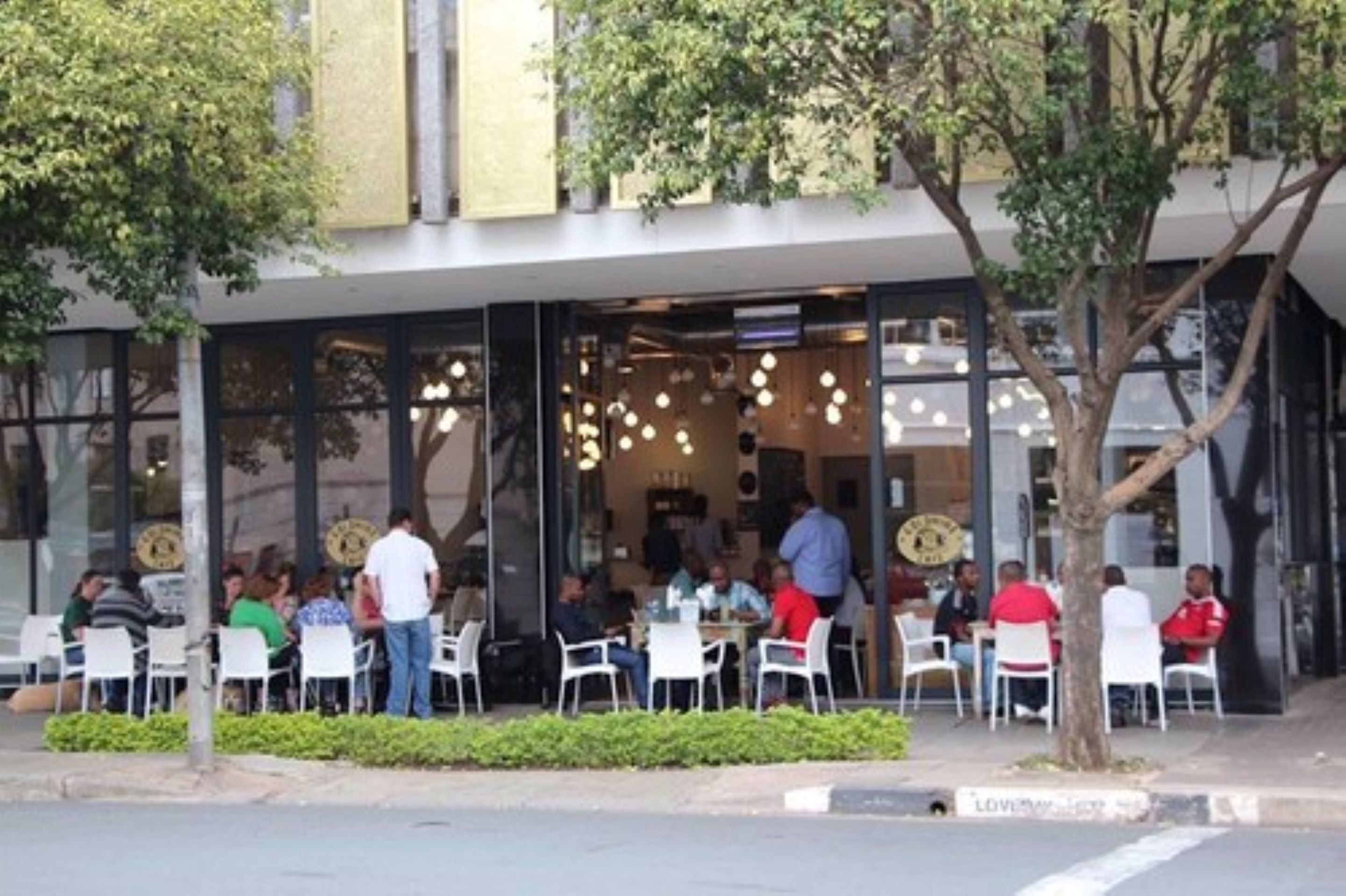 Un espace extérieur aménagé avec des tables et des chaises, un bâtiment doté de grandes fenêtres et un arbre au premier plan.