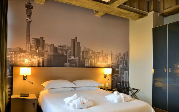 Una habitación de hotel con una cama, dos lámparas de noche, una mesita de noche, una silla y un armario.