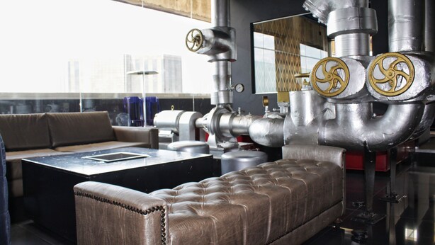 Una sala de estar moderna con un sofá de cuero, una mesita de centro y tuberías y válvulas de metal de estilo industrial.