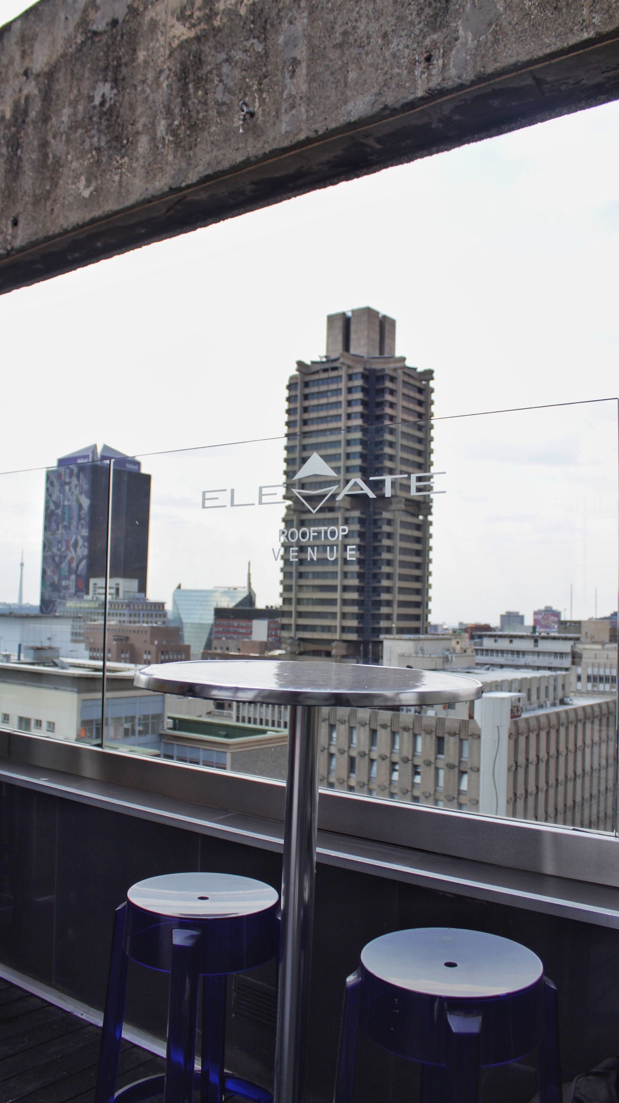 Un edificio alto con un letrero de local en la azotea, dos taburetes y una vista del paisaje urbano a través de una ventana.