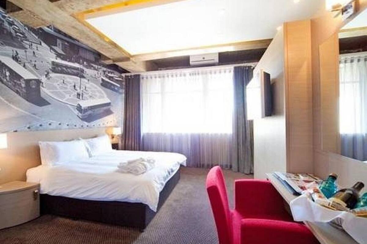 A hotel room with a bed, a desk with a chair, a TV, and a window with curtains.