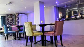 A dining area with a table and chairs, a kitchen in the background, and a tiled floor.