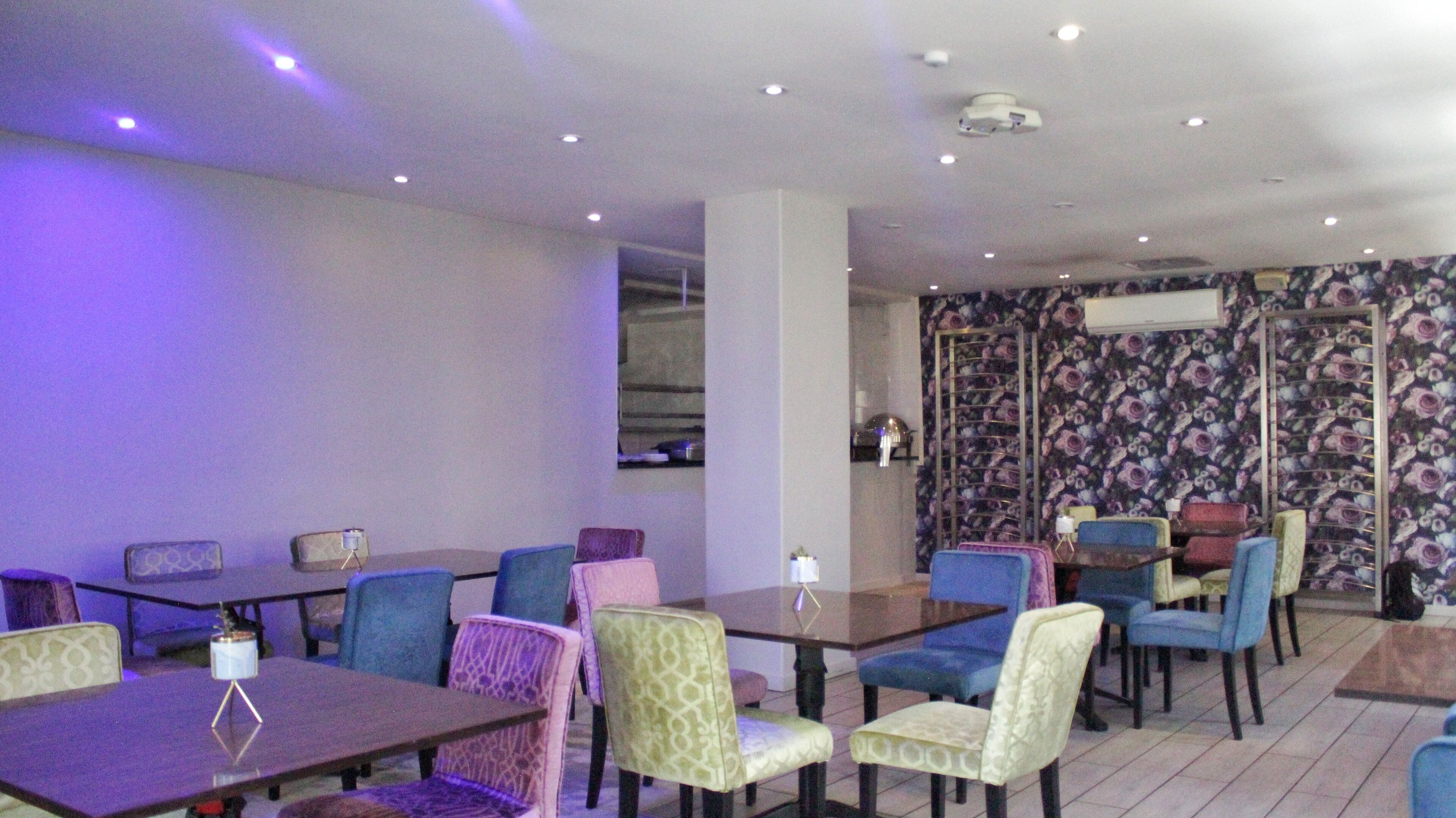 A dining area with multiple tables and chairs, a patterned wall, and ceiling lights.