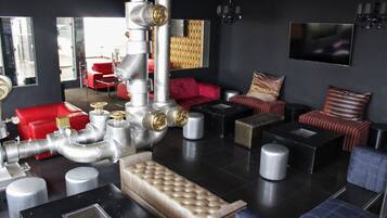Un salón moderno con una fuente de agua de estilo industrial en el centro, asientos rojos y a rayas, y un televisor de pantalla plana montado en la pared.