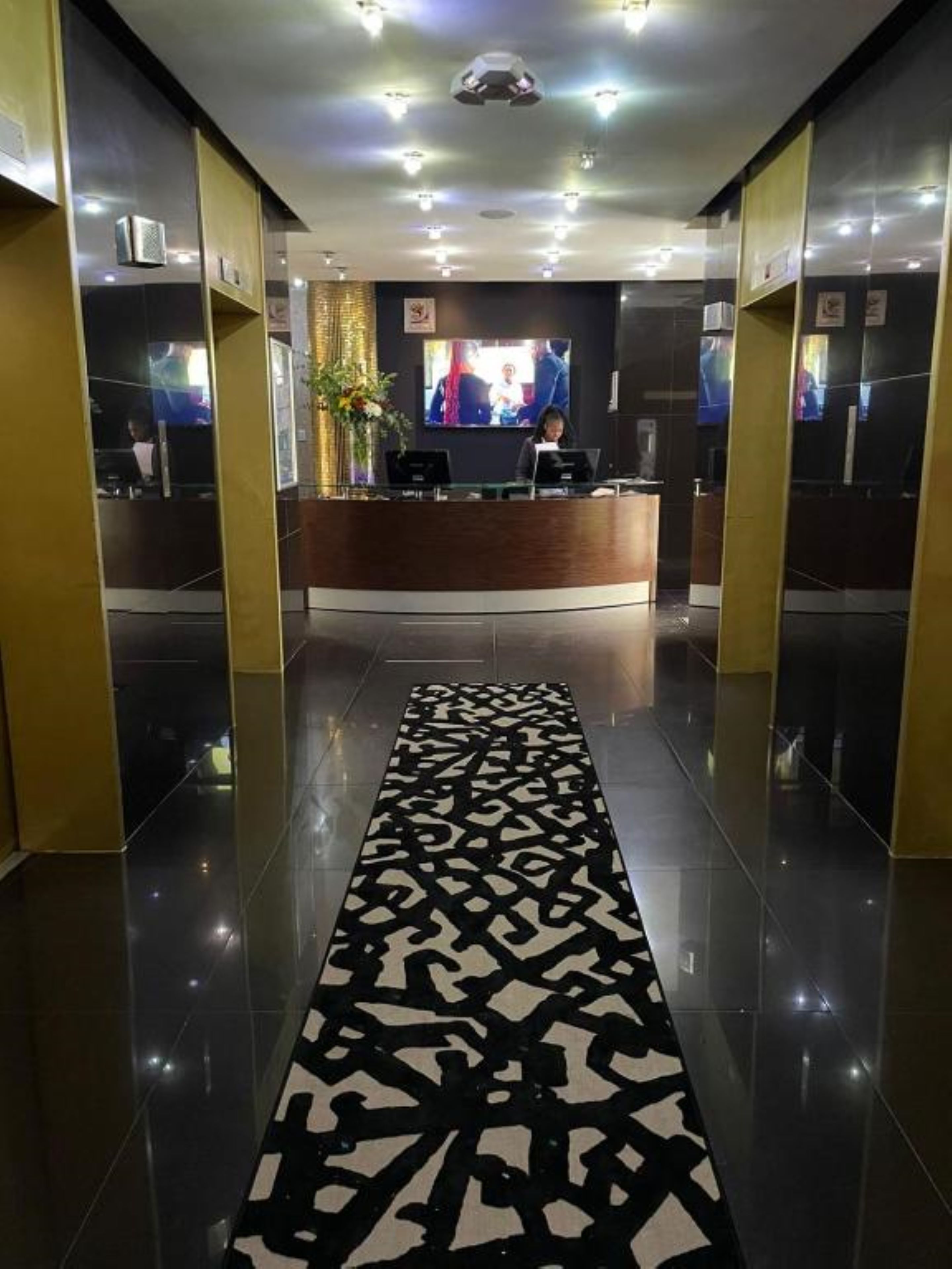 A reception area with a modern design, featuring a reception desk, a flat-screen TV, and a patterned carpet.
