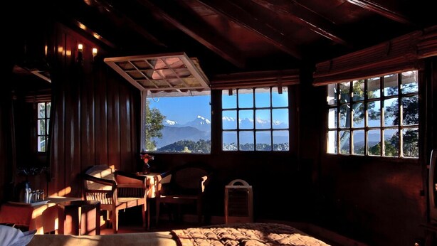 A cozy room with a bed, a desk, and a chair, large windows with a mountain view, and wooden walls.