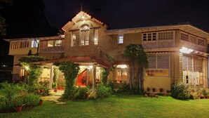 A two-story building with a stone facade, a covered porch with potted plants, and a staircase leading to the upper floor.