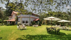 A two-story building with a red roof and white walls, surrounded by lush greenery and outdoor seating areas.