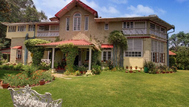 A large, two-story house with a red roof, surrounded by a well-maintained garden with various plants and flowers.