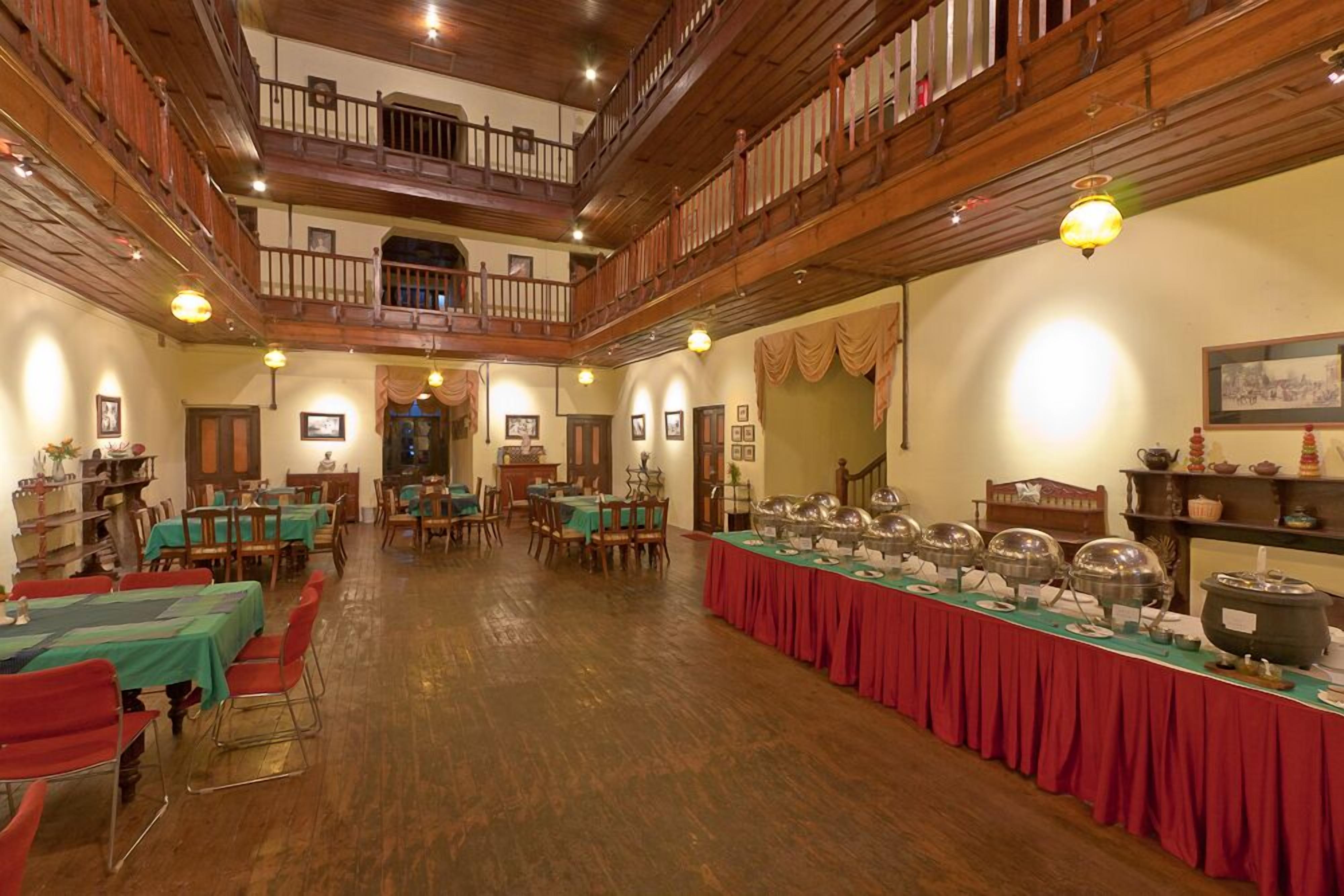 A spacious dining hall with high wooden ceilings and a mezzanine level. Tables are set with green tablecloths and red runners.