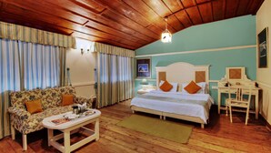 Una habitación acogedora con techo de madera, una cama con ropa blanca y almohadas naranjas, un sofá floral, una mesita con una bandeja de desayuno y un escritorio con una silla.
