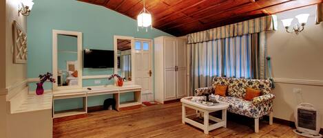 A living room with wooden flooring, a sofa, a TV, a mirror, and a ceiling with wooden beams.
