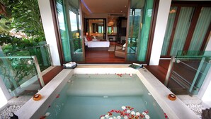 Ein modernes Hotelzimmer mit einer großen Badewanne, einem Bett und Blick auf den Raum durch eine Glastür.