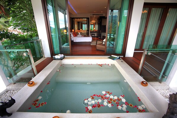 A modern hotel room with a large bathtub, a bed, and a view of the room through a glass door.