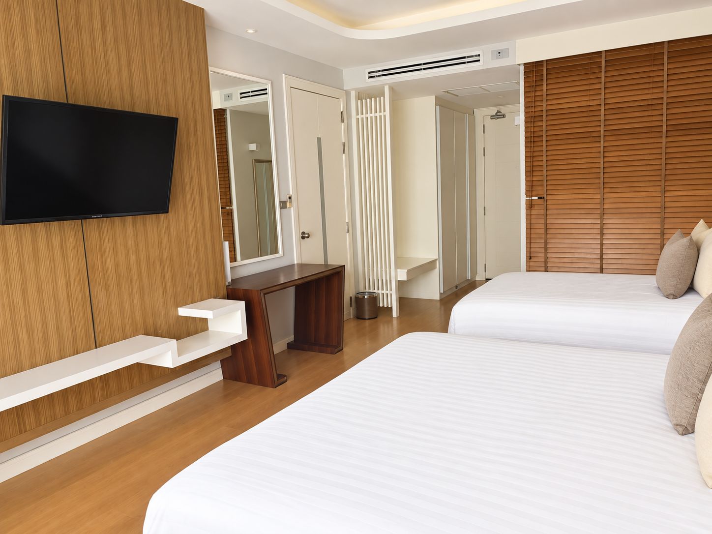 Habitación de hotel con dos camas, televisión, armario de madera y baño con ducha.