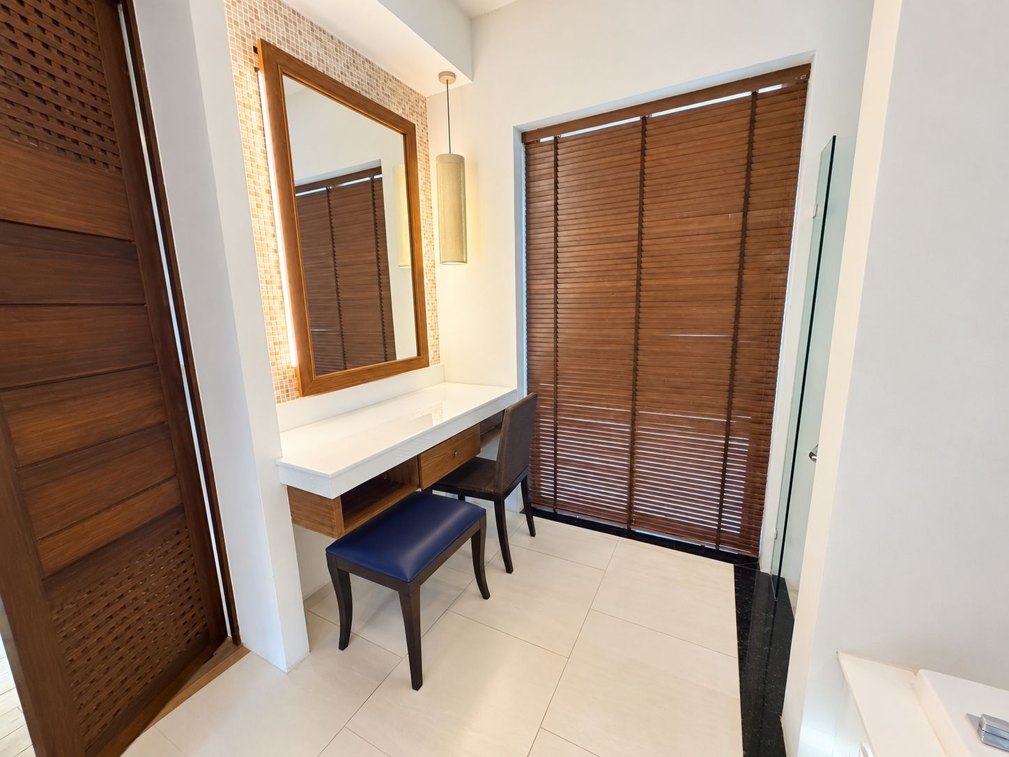 A bathroom with a white vanity, a mirror, a bench, and a sliding door.