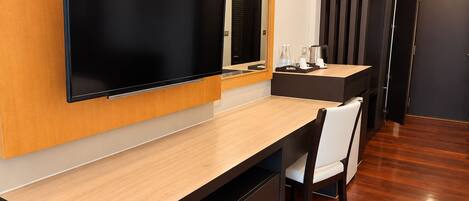 A modern hotel room with a large flat-screen TV mounted on the wall, a wooden desk with a chair, and a small coffee table.
