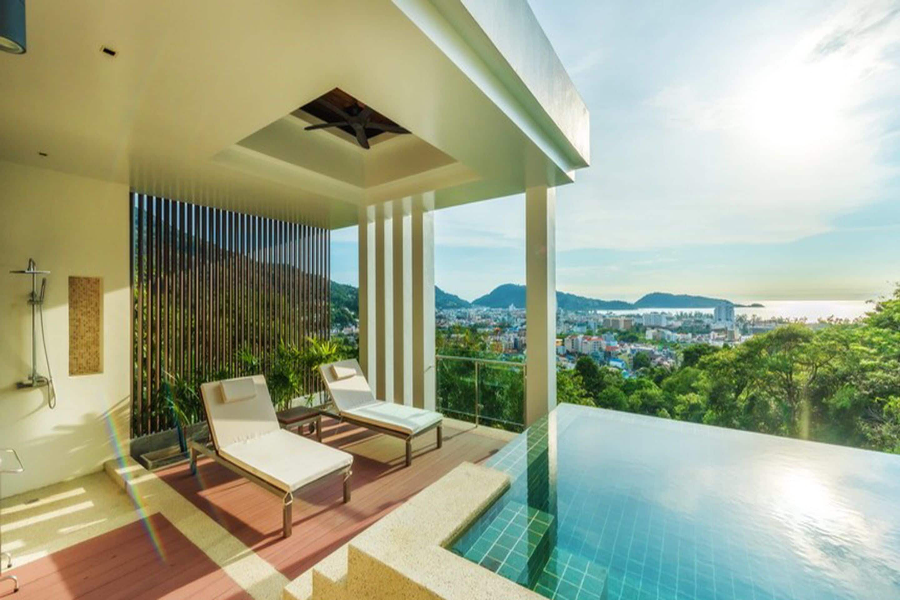 A modern balcony with a pool, two lounge chairs, and a city view.