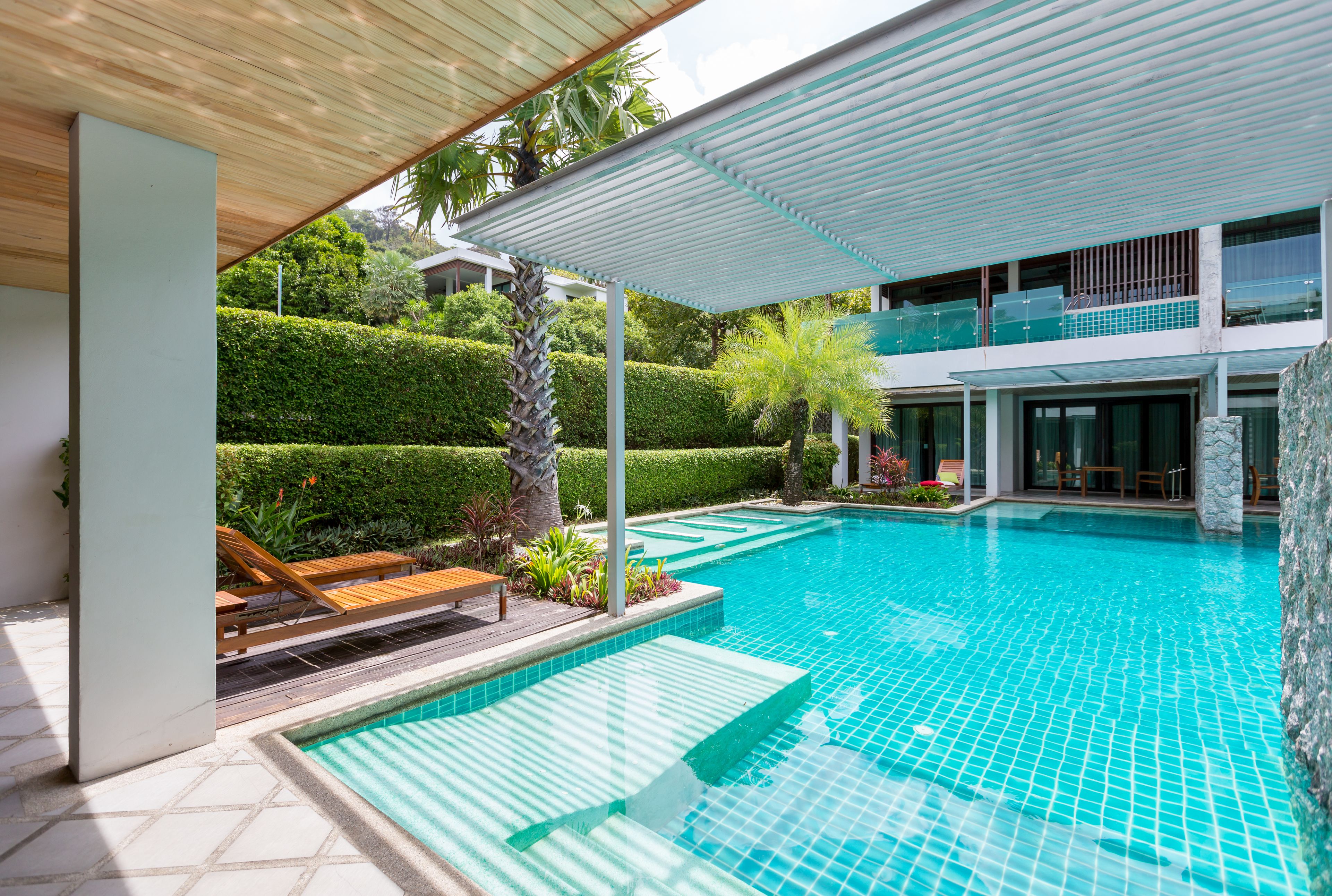 A modern pool area with a clear blue pool, wooden lounge chairs, and a covered seating area.