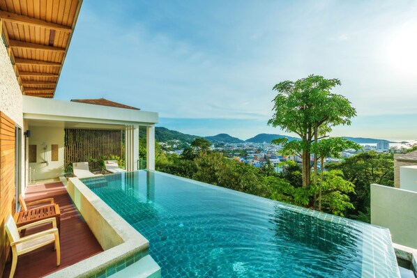 Relax by the infinity pool overlooking a lush landscape and distant cityscape.