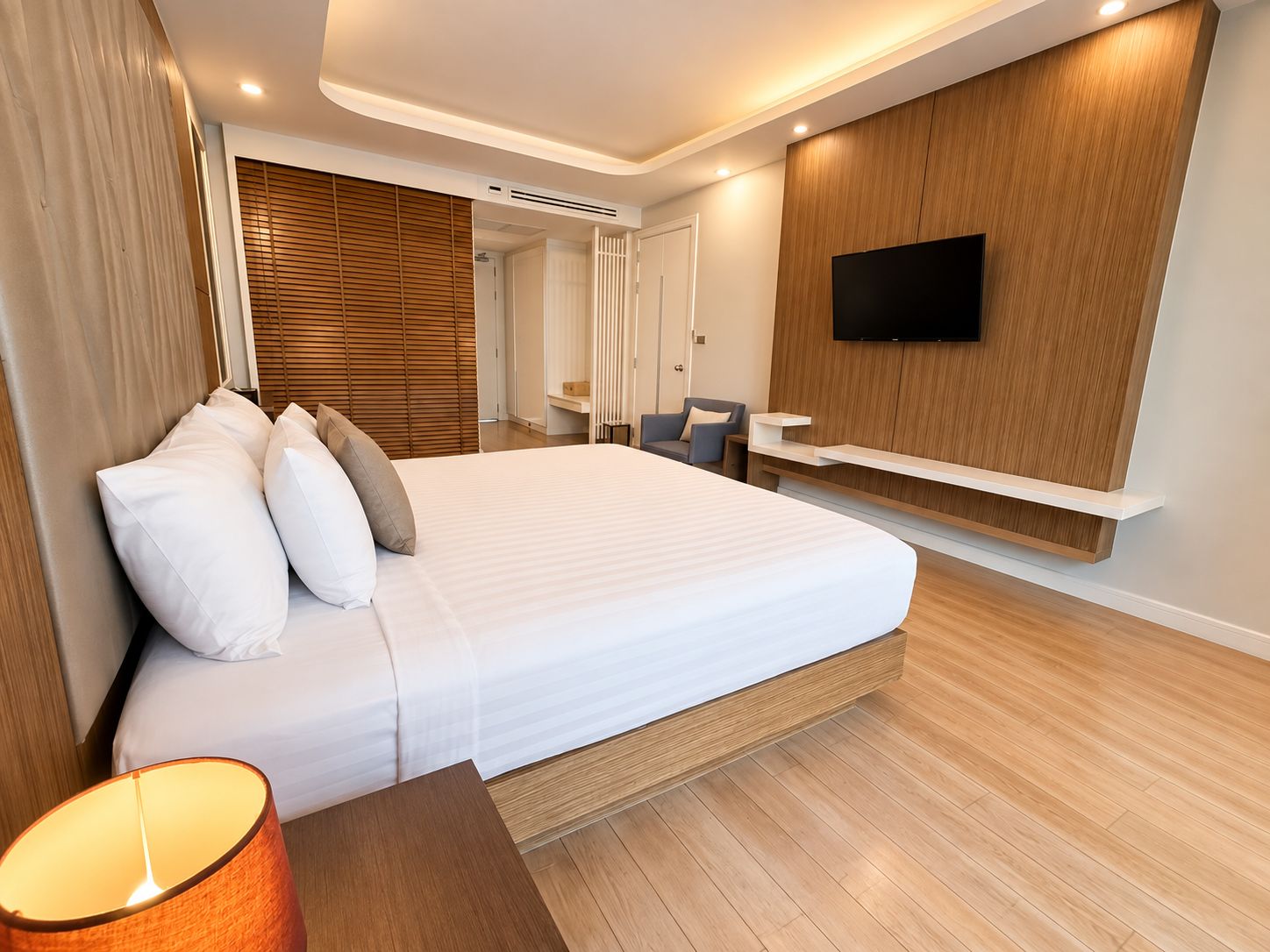 A modern hotel room with a large bed, a flat-screen TV mounted on the wall, and a desk with a chair.