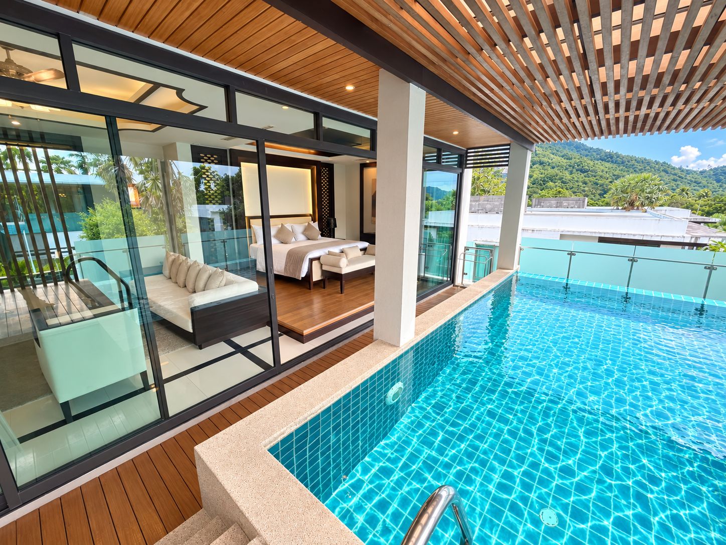 A modern hotel room with a glass wall, a pool, and a view of the mountains.