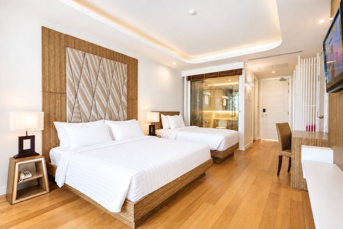 Una habitación de hotel moderna con una cama grande, mesitas de noche, un escritorio y zona de ducha.