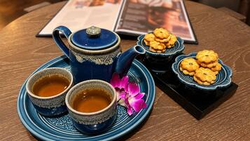 Uma mesa com um bule azul, duas xícaras de chá, um prato de biscoitos e uma flor rosa.