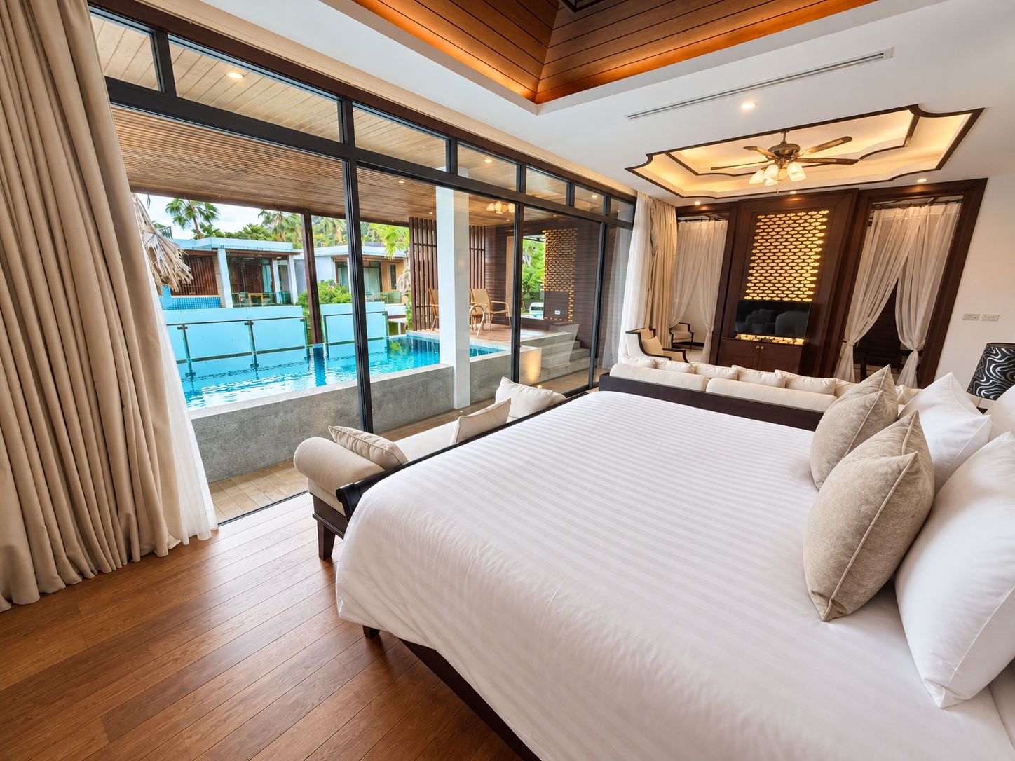 A spacious bedroom with a large bed, a view of a swimming pool, and a modern ceiling design.