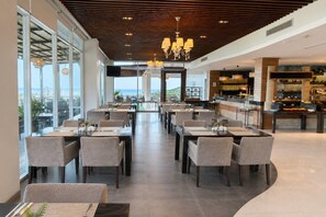 A modern restaurant with a view of the ocean, featuring a long dining area with tables and chairs, a bar area, and a high ceiling with wooden beams. - Club Wyndham Patong Hill, Trademark Collection by Wyndham (Patong)