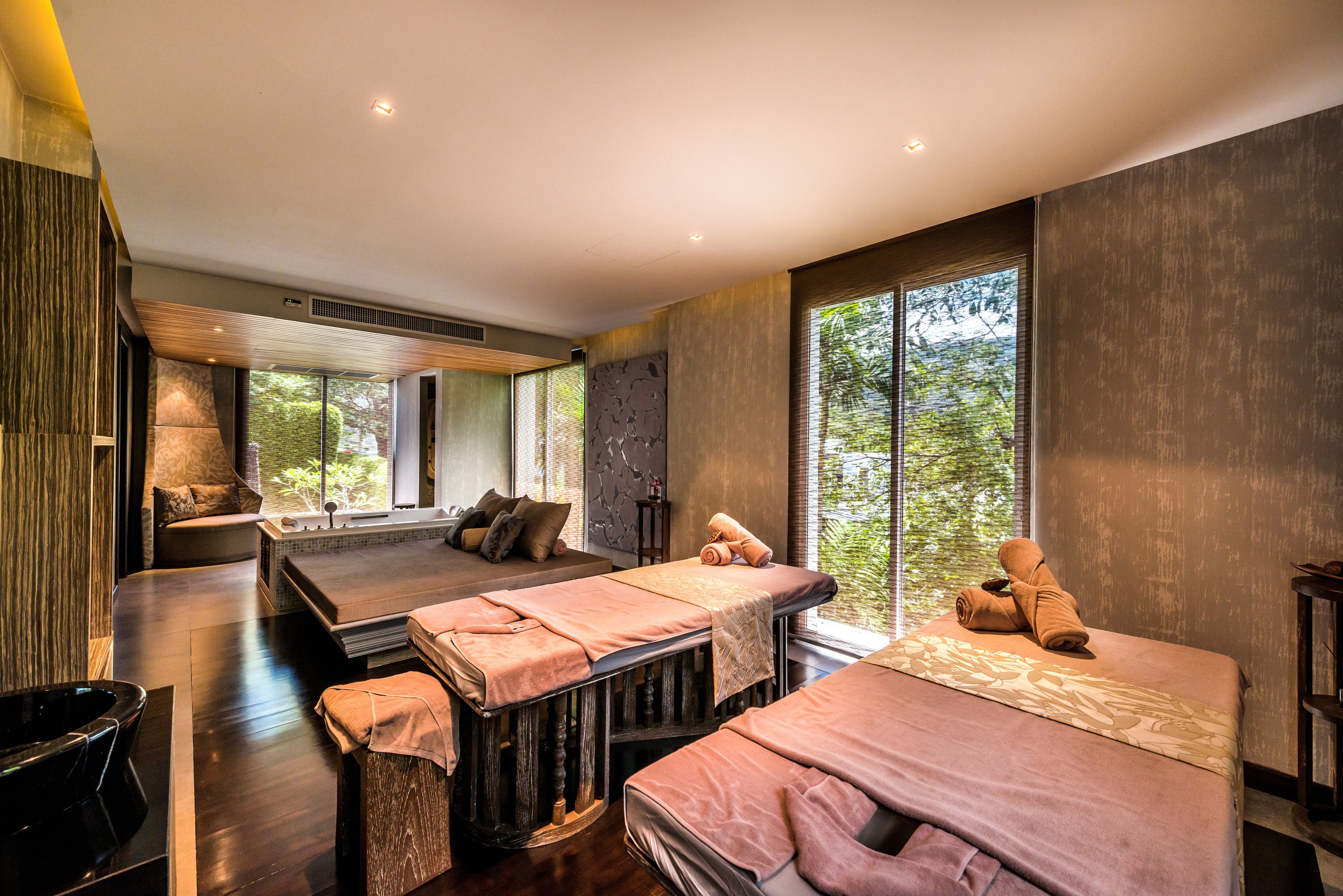 Une salle de spa équipée de deux tables de massage, d’une grande fenêtre donnant sur la forêt et d’un mur en pierre.