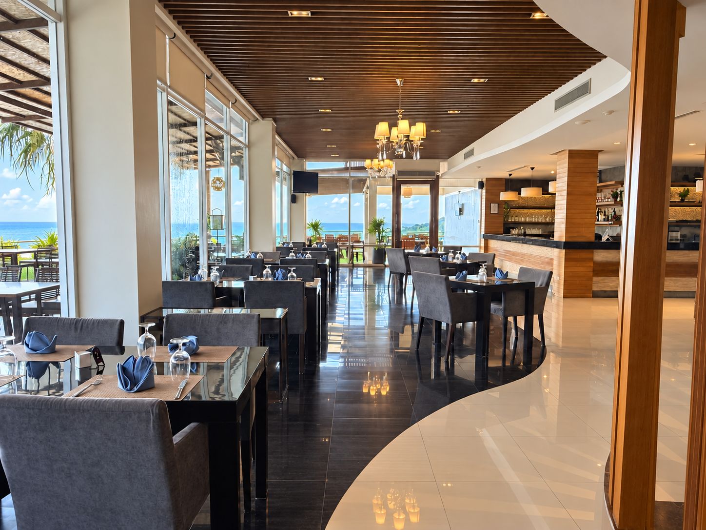 Un restaurant modern amb vista a l'oceà, que destaca per una àrea de menjador ampla amb taules i cadires, una zona de bar i un sostre de fusta.