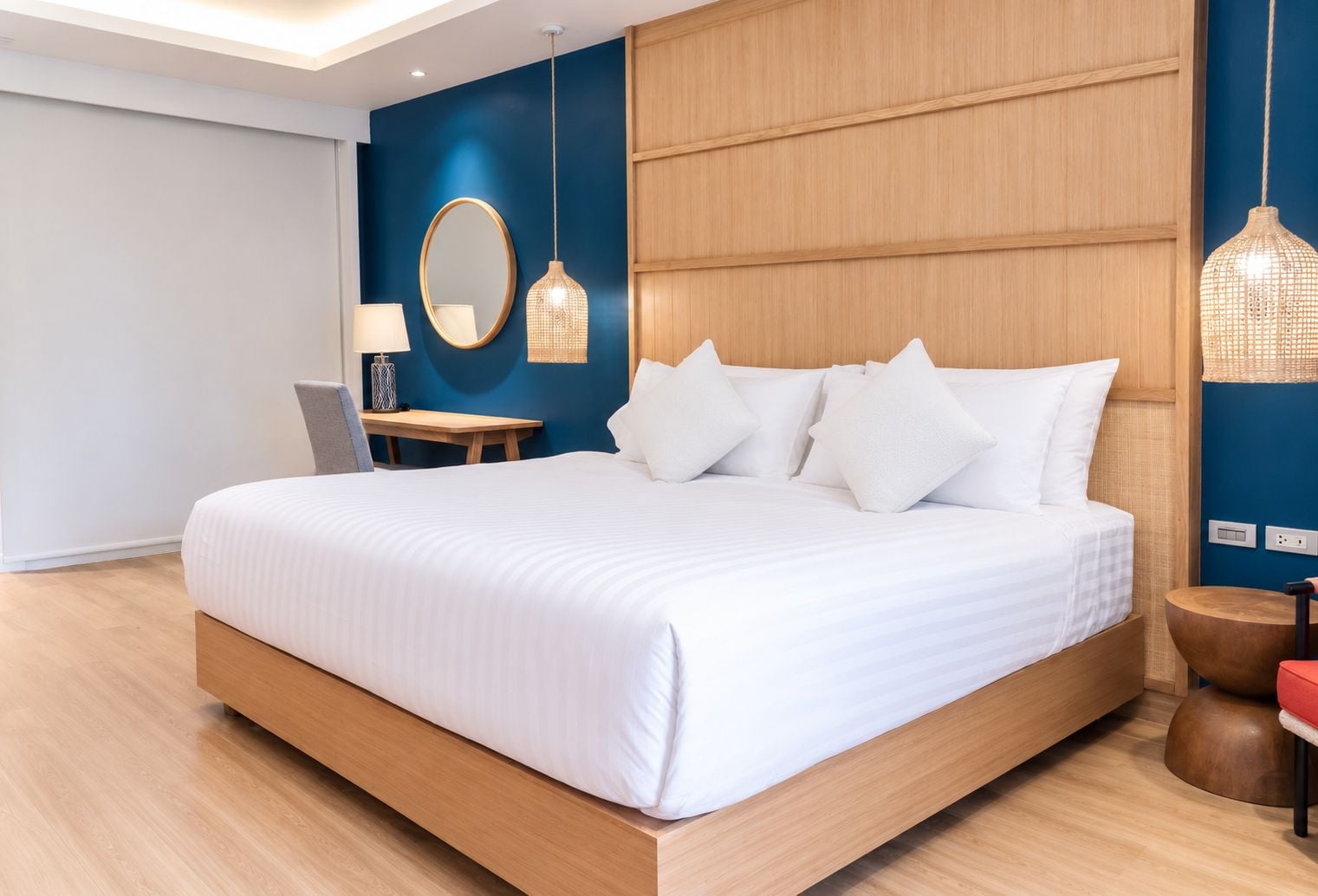 Una habitación de hotel moderna con una cama grande, un escritorio y una silla. Hay un espejo en la pared y una lámpara colgante.