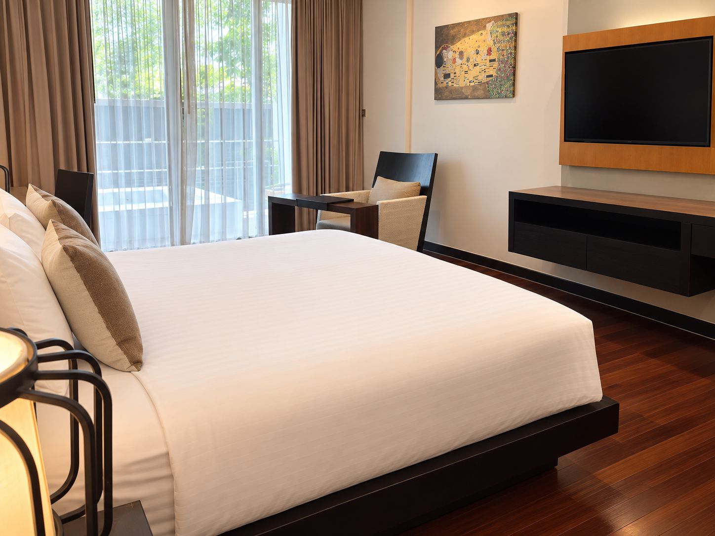 Una habitación de hotel con una cama grande, un televisor instalado en la pared y una puerta corrediza que da a un balcón.