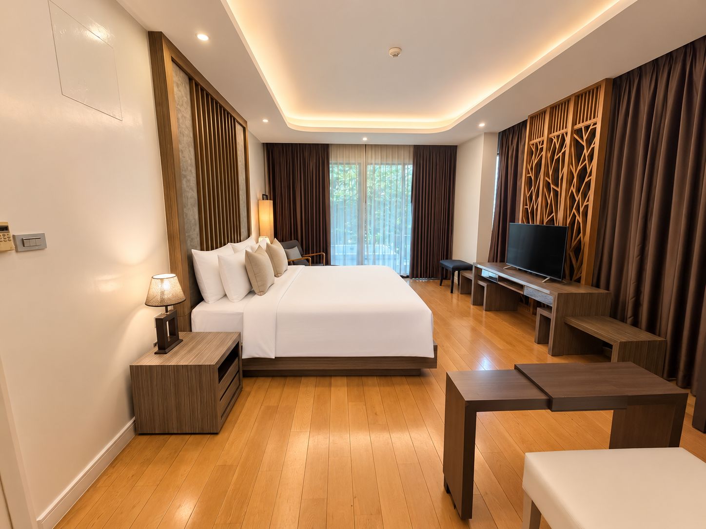 A modern hotel room with a large bed, a desk, a TV, and a view of the outdoors.