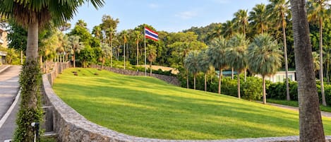 A landscaped area with a stone wall, palm trees, and a flag.