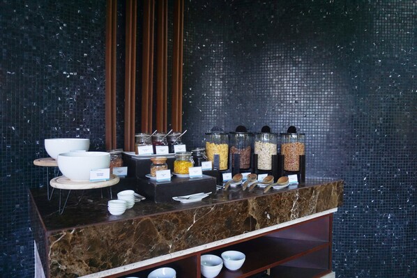 A buffet setup with bowls, jars, and utensils on a marble counter against a tiled wall.