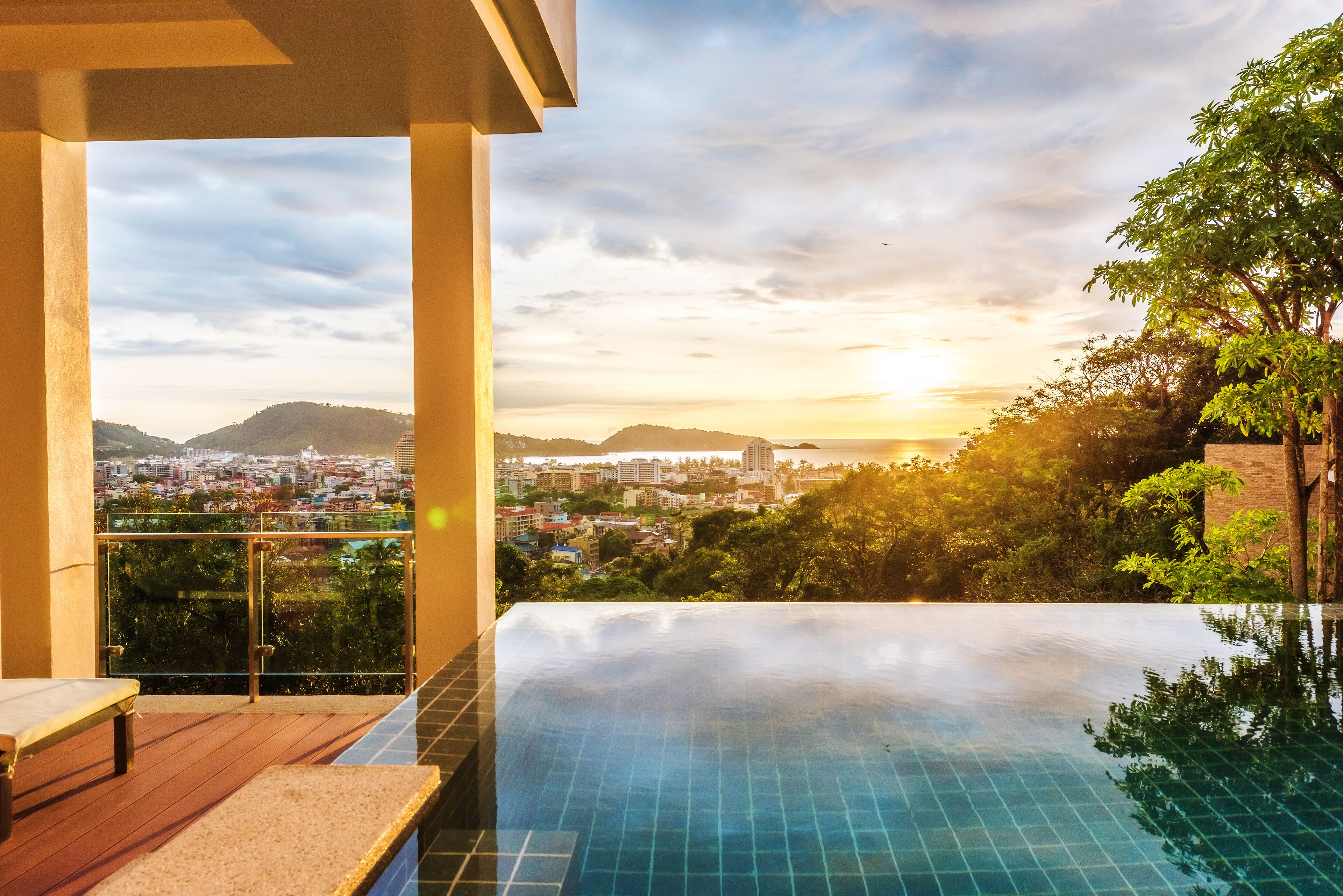 A rooftop infinity pool with a cityscape view, a wooden deck, and a glass balustrade.