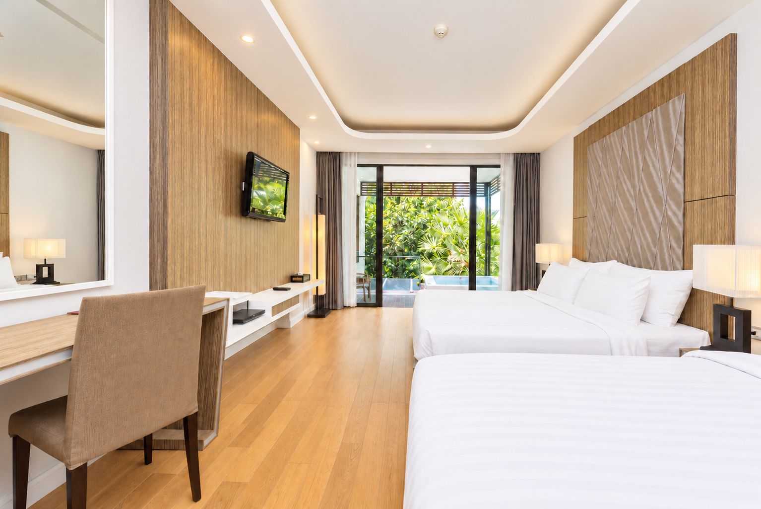 Habitación de hotel con cama, escritorio, silla, televisor y vista a zonas verdes.