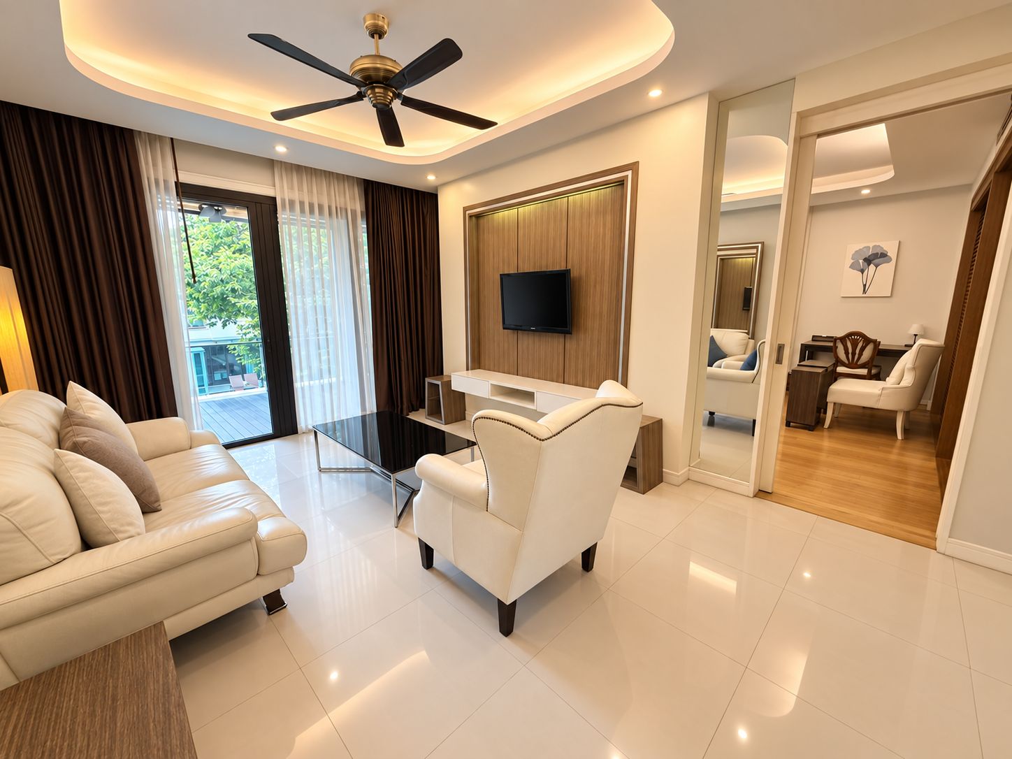 A modern living room with a sofa, a glass coffee table, a ceiling fan, and a TV mounted on the wall.
