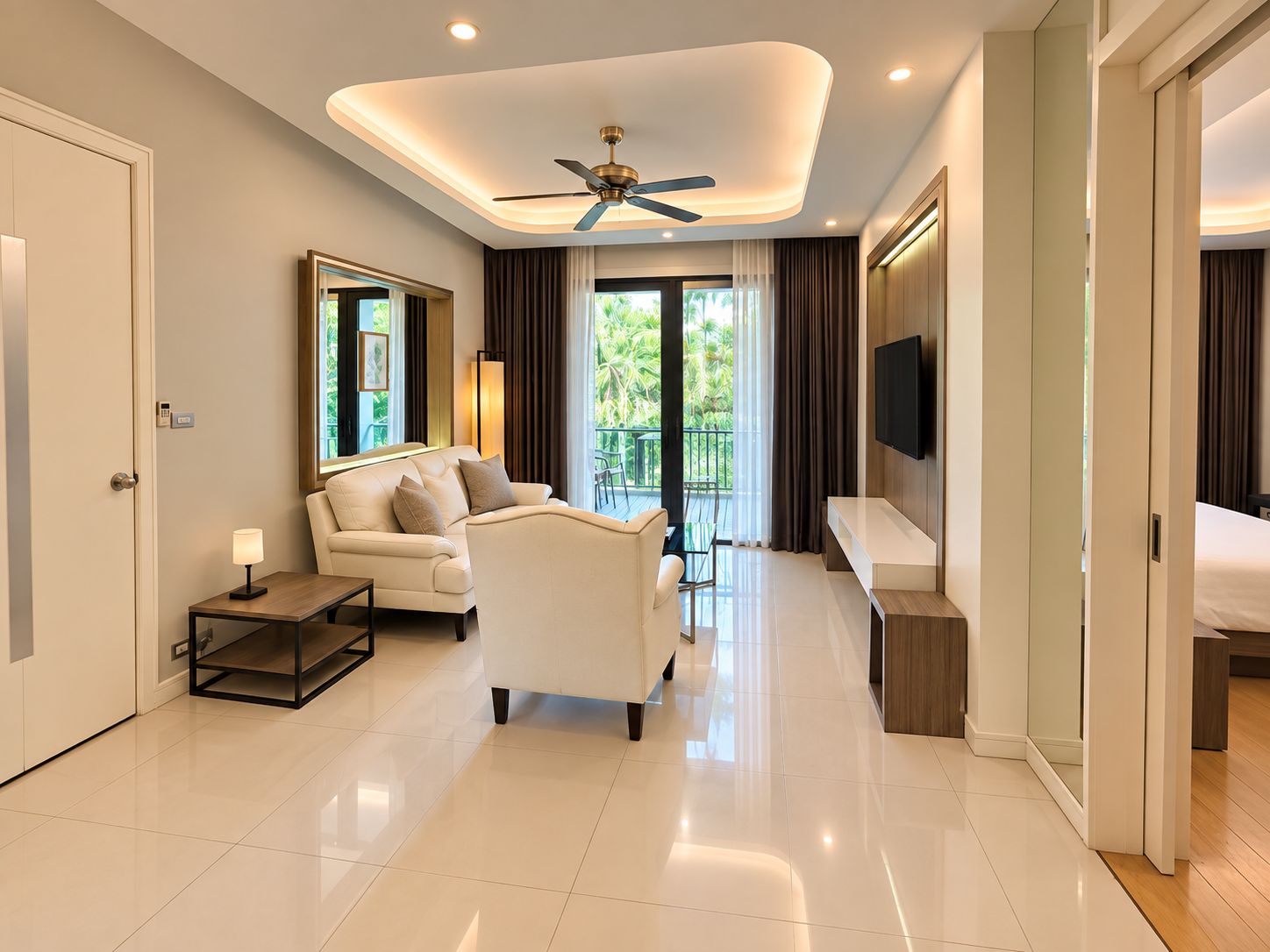 A modern hotel room with a sofa, a TV, a ceiling fan, and a balcony with a view of greenery.