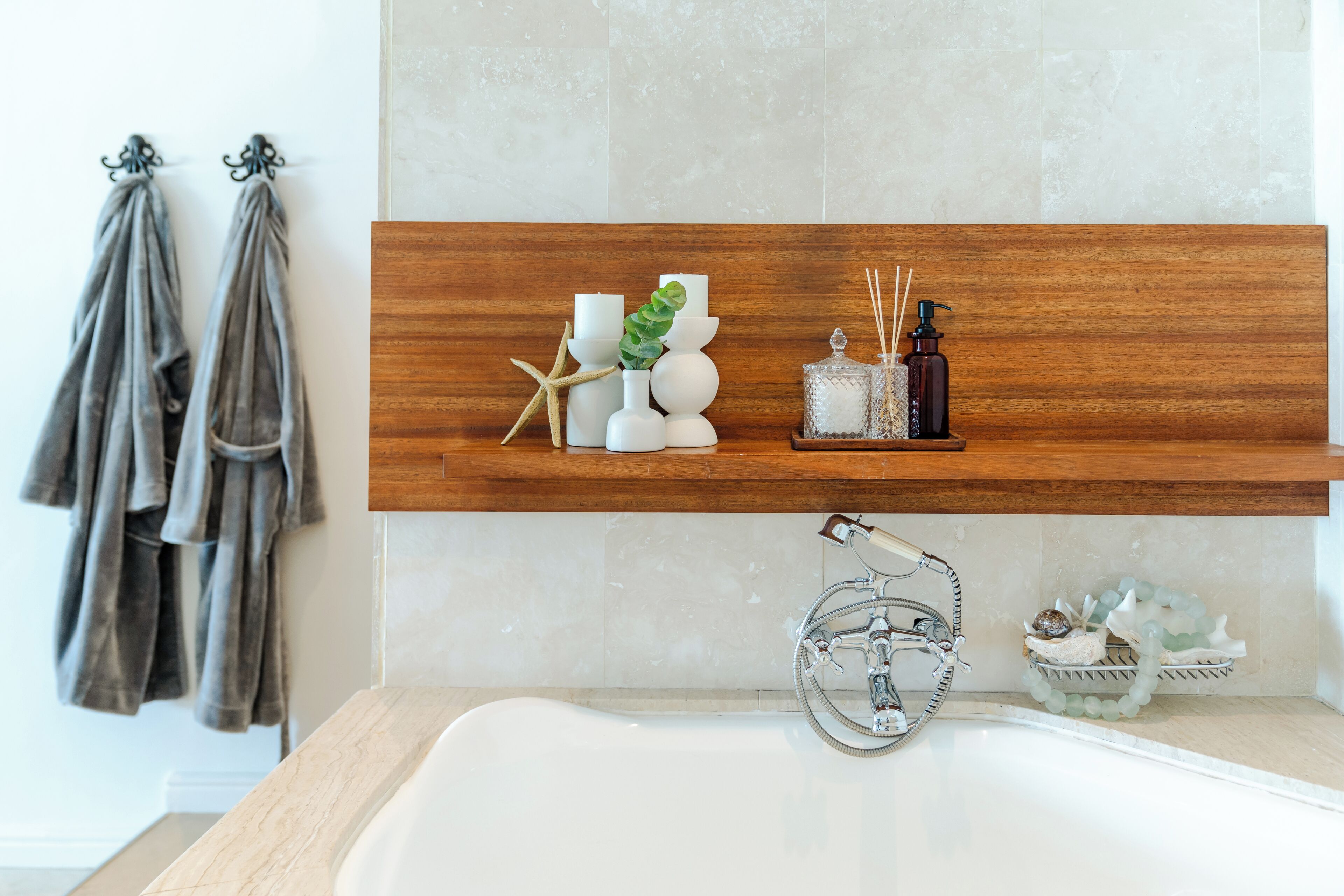 A bathroom with a wooden shelf holding candles, a starfish, and toiletries. There are towels hanging on hooks to the left.