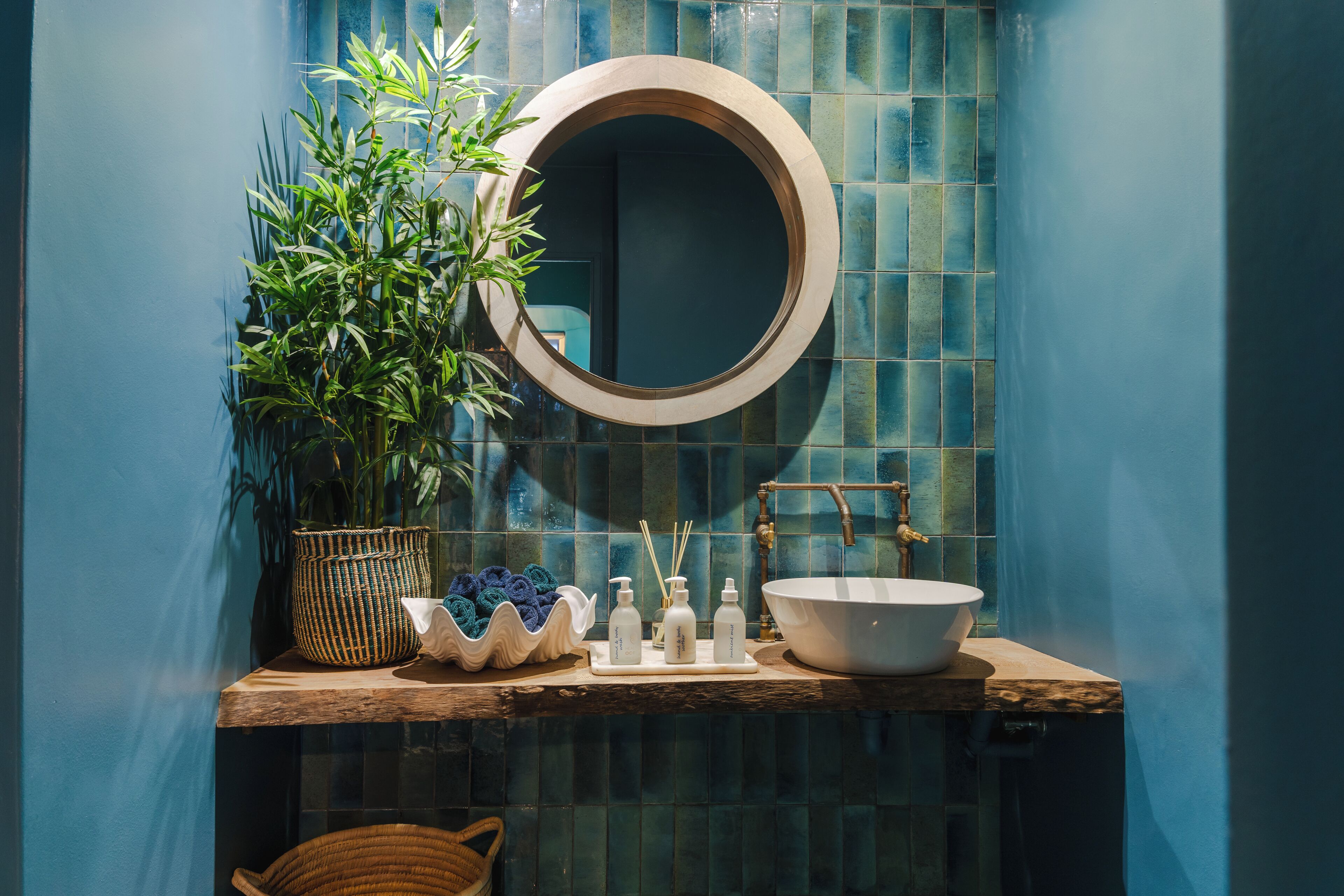 Une salle de bain avec un miroir rond, un lavabo et une plante en pot.