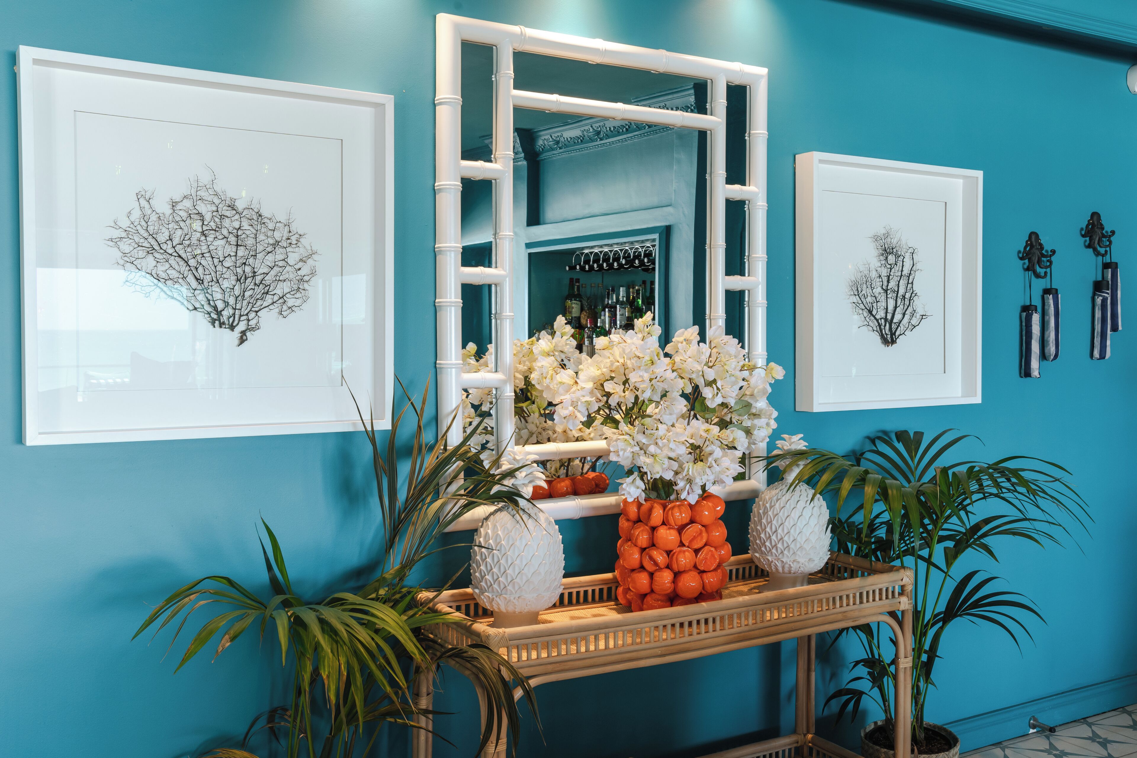 Pared azul con impresiones botánicas enmarcadas, un espejo y una consola decorada con objetos ornamentales.