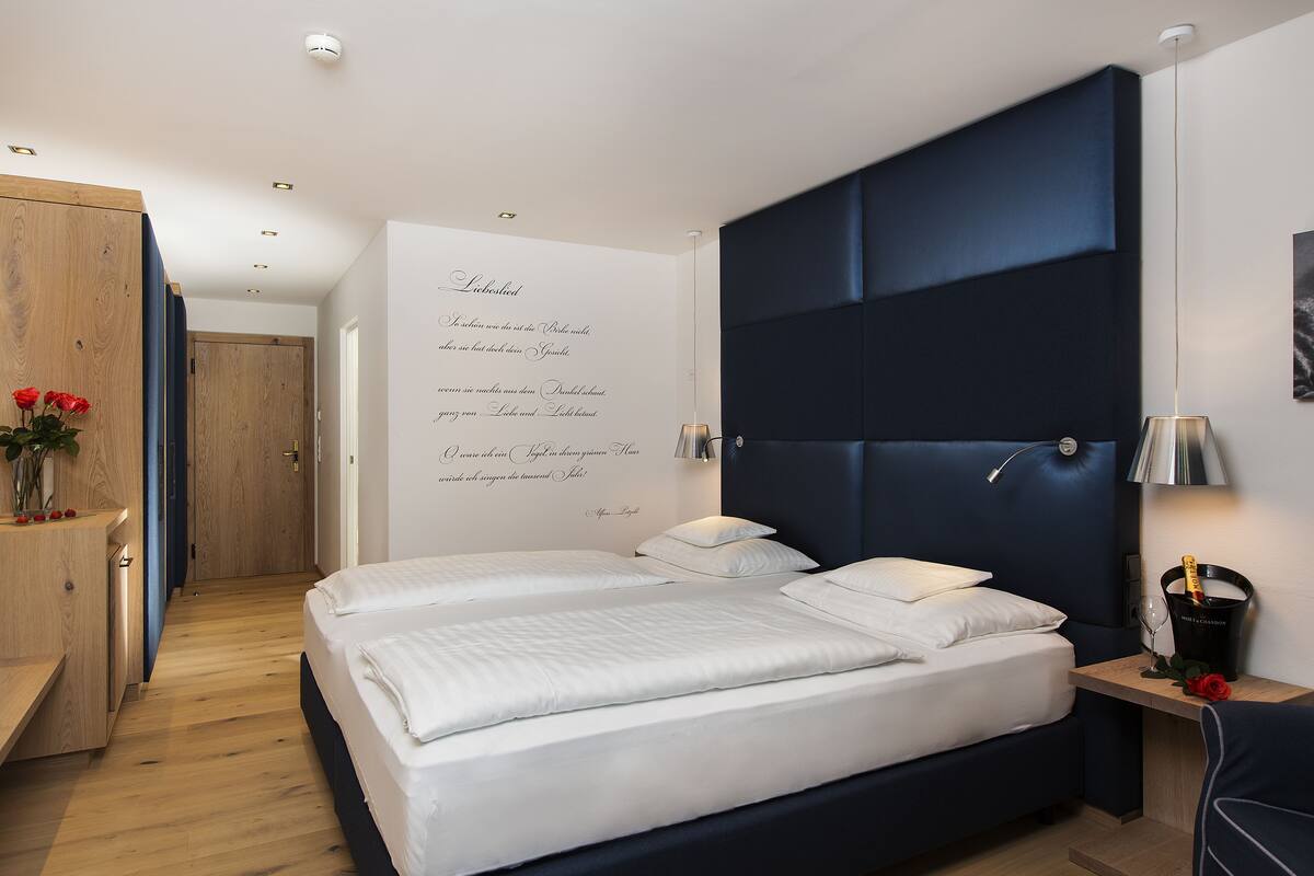 A modern bedroom with a large bed, a wooden dresser, and a wall with decorative text.