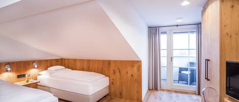 A modern bedroom with a loft-style ceiling, wooden panel walls, a large bed, a TV, and a sliding glass door to a balcony.